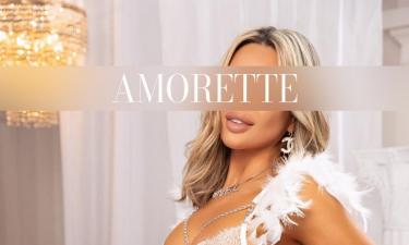 Elite Escort Model Chloe from Vienna with blonde hair, sitting on the bed in white lingerie