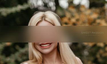 SP Escort Agency Munich, Carolin in a rose Dirndl. Her blond hair is falling over her shoulder while she stands in a garden.